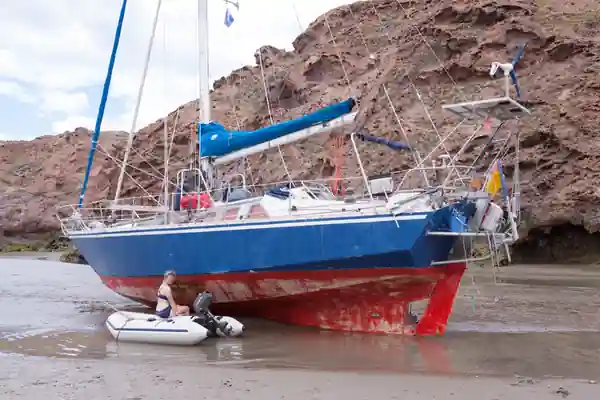 Voilier de voyage Fleur de Sel à l'échouage sur un fond meuble entouré d'un paysage rocailleux.
Devant le bateau, son annexe posée sur le sable.