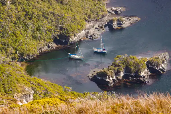 Deux voiliers de voyage en Terre de Feu. En plus de leur ligne de mouillage, on devine les nombreuses lignes à terre qui permettent de les sécuriser entre un îlot et la terre, dans une caleta (crique) bien protégée.