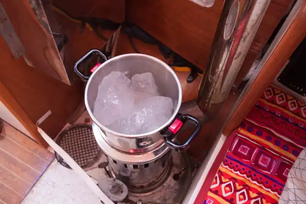 Cocotte-minute remplie de glace en train de fondre sur un poêle à gazole dans le carré d'un bateau.