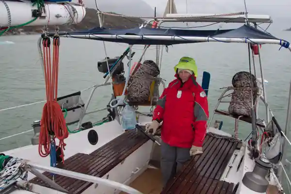 Cockpit du voilier de voyage Fleur de Sel, par un temps bouché et humide. La barreuse est à l'abri d'un taud et on devine, amarrés dans le balcon arrière, deux sacs en filet, qui contiennent de longues aussières flottantes.