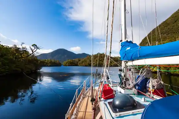 Vue du cockpit du voilier de voyage Fleur de Sel vers l'avant. On devine une amarre flottante sur bâbord et sur son pont sont arrimés des jerrycans de carburant. Les nuages se dégagent et laissent la place à une belle éclaircie qui illumine le voilier.